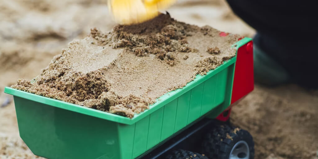 child playing with sand and a toy digger