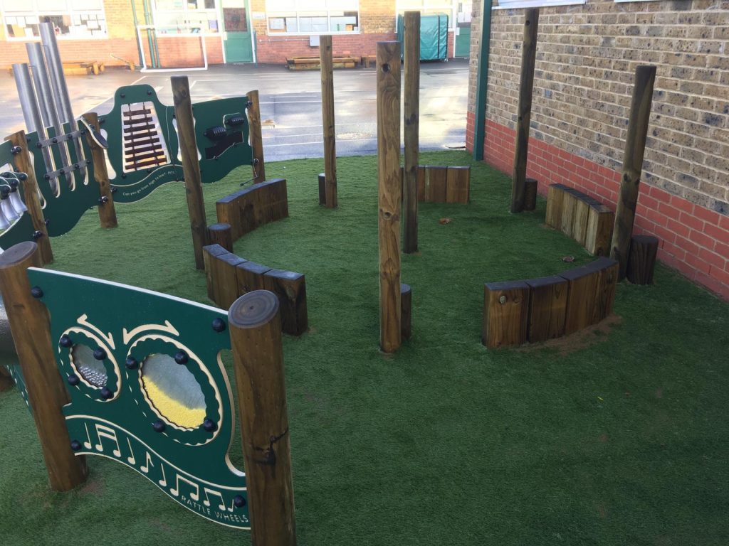 Green Frog Artificial Grass used as safety surfacing for a primary school trim trail and musical play set playground equipment.